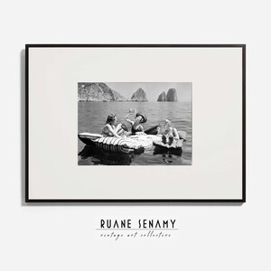 Peut inclure: Photographie en noir et blanc de trois personnes sur un radeau dans l'eau. Les personnes sourient et semblent s'amuser. La photo est encadr&eacute;e dans un cadre noir.