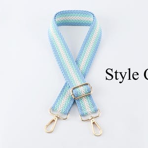 K&ouml;nnte beinhalten: Ein gewebter Taschenriemen in hellblau und wei&szlig; mit goldenen Beschl&auml;gen. Der Riemen ist in der Mitte gefaltet und die Enden des Riemens sind mit goldenen Verschl&uuml;ssen verbunden. Der Text "Style C" ist auf dem Bild zu sehen.