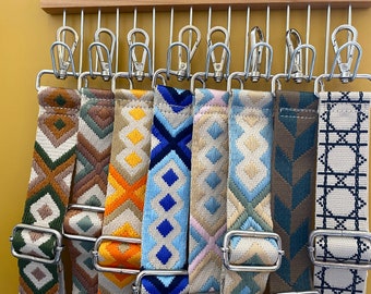 May include: Nine colorful patterned fabric straps with silver clasps hanging on a wooden rack. The straps have geometric designs in shades of brown, green, orange, blue, and white.