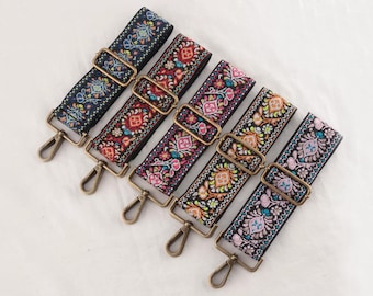May include: Six colorful embroidered bag straps with floral patterns. Each strap features a different color scheme, including navy, red, pink, and purple, with gold-colored metal hardware and clasps. The straps are arranged diagonally on a white surface.