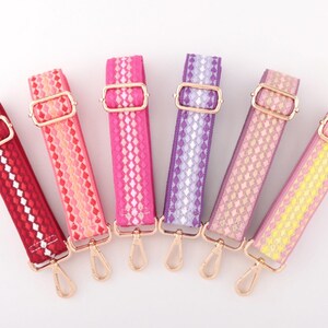 Pode incluir: Seis alças de bolsa tecidas coloridas em tons de vermelho, rosa, roxo e amarelo. Cada alça apresenta um padrão geométrico, ferragens de metal dourado e um fecho giratório. As alças são projetadas para uso com bolsas ou outros acessórios.