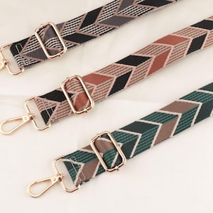 Op de afbeelding: Drie patroon tasriemen met goudkleurige metalen hardware. De riemen hebben geometrische ontwerpen in zwart, grijs, bruin en groen. Elke riem heeft een rechthoekige gesp en een draaibare sluiting.