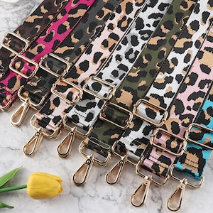 Könnte beinhalten: Ein Set aus zehn bunten, verstellbaren Riemen mit Leopardenmuster und goldenen Metallschließen. Die Riemen sind aus gewebtem Stoff und haben eine Vielzahl von Farben, darunter Pink, Blau, Grün und Schwarz.