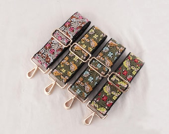 May include: A collection of five decorative bag straps with floral embroidery. The straps feature a black base with colorful embroidered flowers and gold-colored metal hardware, including adjustable buckles and swivel clasps.