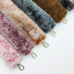 May include: A collection of faux fur accessories in various colors, including pink, burgundy, tan, gray, and brown. Each piece has a gold-colored clasp attached. The items are arranged diagonally against a white background.