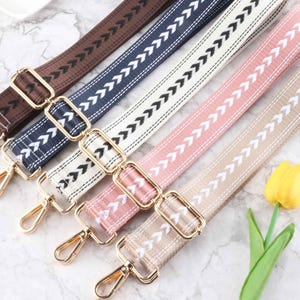 Peut inclure: Cinq sangles en tissu de couleurs différentes avec des fermoirs en métal doré. Les sangles ont un motif en chevron avec des coutures blanches.
