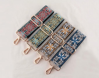 May include: An assortment of colorful, patterned bag straps. Each strap features a different design with floral and geometric motifs in shades of red, blue, yellow, and white. Gold-colored metal hardware includes adjustable buckles and swivel clasps.
