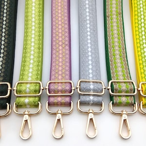 May include: Six colorful bag straps with gold-tone hardware. The straps are in shades of black, green, purple, gray, and yellow. Each strap features a diamond pattern with a contrasting color. The straps have gold-tone rectangular buckles and swivel clasps.