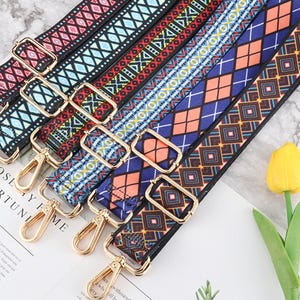 Op de afbeelding: Assortiment van kleurrijke, gepatroneerde stoffen banden met gouden metalen gespen. De banden zijn geweven met geometrische patronen in tinten rood, blauw, groen en bruin.