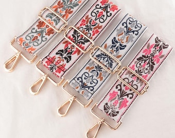 May include: Four decorative bag straps with floral patterns in orange, red, gray, and pink on a white background. Each strap has gold-colored metal hardware, including adjustable buckles and clasps. The straps are designed for handbags or other accessories.