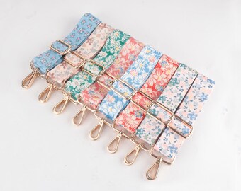 Könnte beinhalten: Eine Sammlung farbenfroher Handtaschenriemen mit floralem Muster. Jeder Riemen weist ein anderes Farbschema auf, darunter Blau, Rosa, Grün und Rot, mit goldfarbener Metallhardware. Die Riemen sind für Handtaschen oder anderes Zubehör bestimmt.
