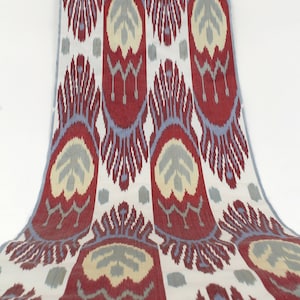 Pu&ograve; includere: Tessuto a motivi rossi, blu e crema con un design ikat. Il tessuto ha uno sfondo bianco con un motivo ripetitivo di fiori e foglie stilizzati.