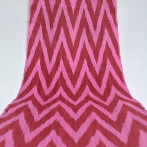 Op de afbeelding: Roze en rode stof met een chevron-patroon. De stof is geweven met een subtiele textuur.