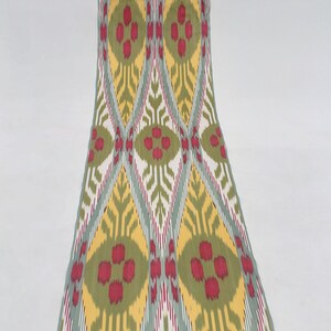 May include: A fabric swatch with a repeating pattern of green, yellow, red, and white diamonds and ovals. The fabric has a woven texture.