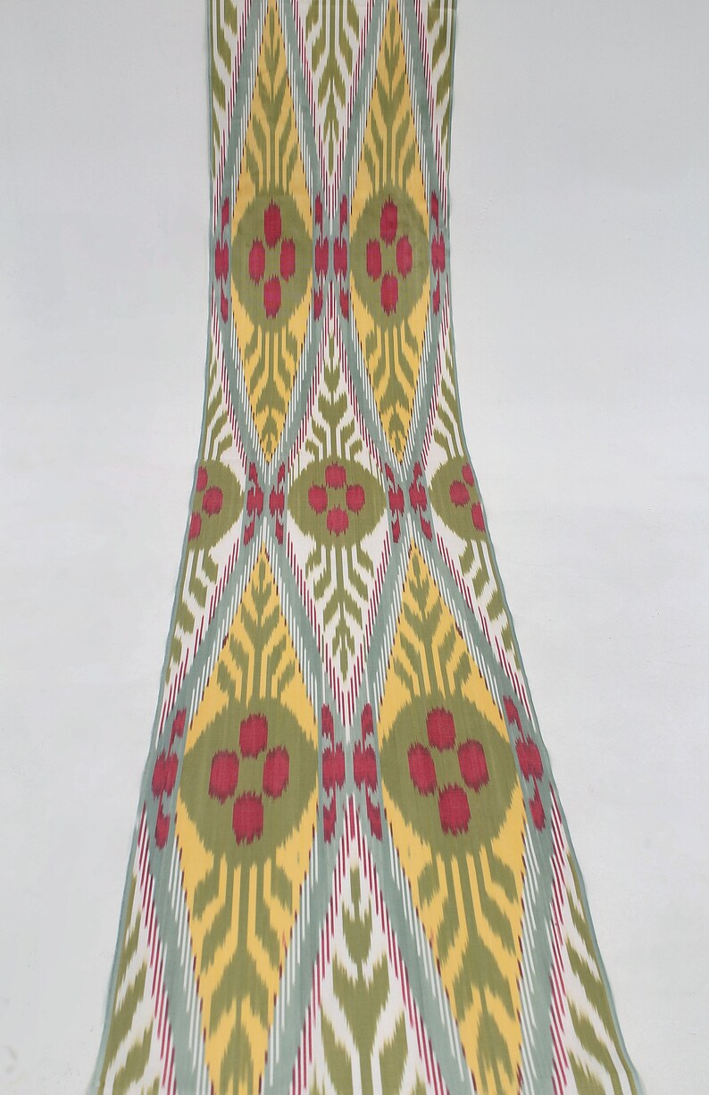 May include: A fabric swatch with a repeating pattern of green, yellow, red, and white diamonds and ovals. The fabric has a woven texture.