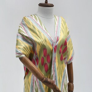 May include: A yellow, green, and red patterned kaftan with a V-neckline. The kaftan is displayed on a wooden mannequin.