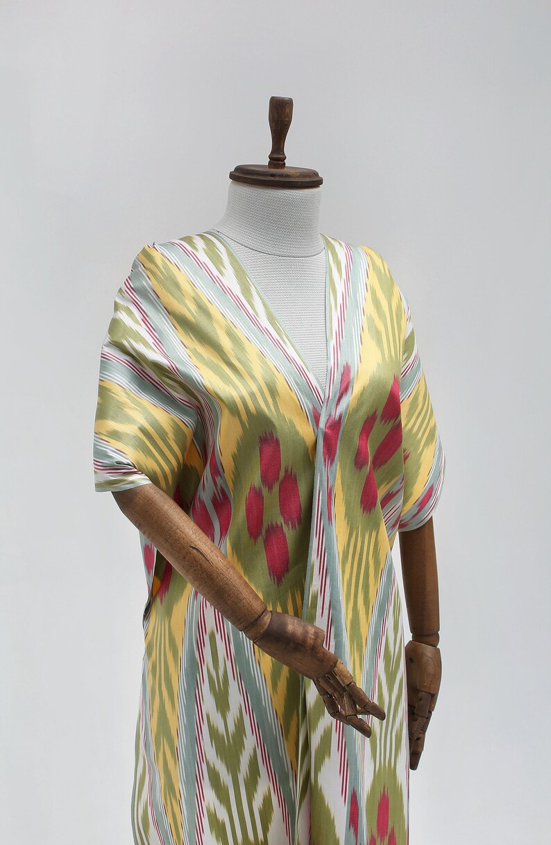 May include: A yellow, green, and red patterned kaftan with a V-neckline. The kaftan is displayed on a wooden mannequin.