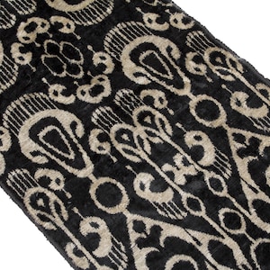 May include: Black and beige patterned fabric with a velvet texture. The design features repeating teardrop and circular shapes with a detailed, textured appearance. The fabric is angled, showcasing the intricate pattern and contrasting colors.
