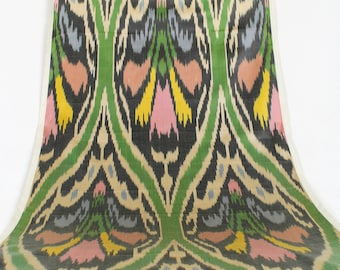 May include: A close-up of a green, black, and beige fabric with a repeating pattern of stylized flowers. The fabric has a subtle sheen and a soft texture.
