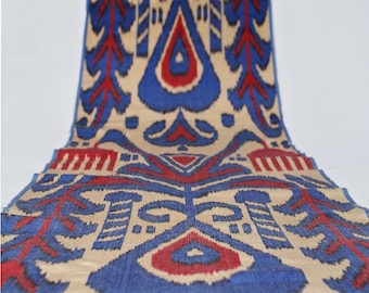 Peut inclure: Gros plan sur un tissu beige avec un motif ikat bleu et rouge. Le tissu a une texture tissée et un design traditionnel.
