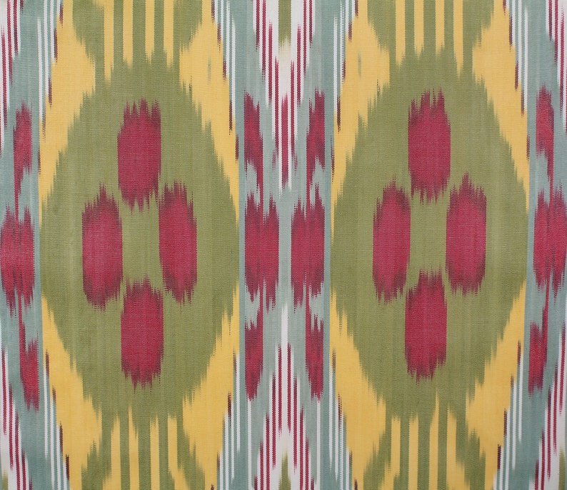 May include: A close-up of a fabric with a repeating pattern of red, yellow, green, and blue. The pattern is a traditional ikat design.