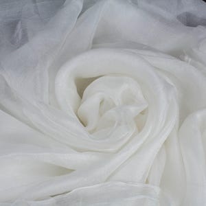 May include: A close-up shot of white fabric, possibly silk or organza, with a soft, flowing texture. The fabric is arranged in swirling folds, creating a sense of depth and movement. The color is a bright, clean white.