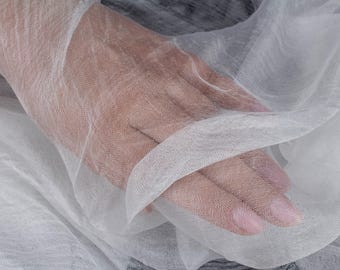 May include: A sheer, lightweight white fabric with a fine, semi-transparent weave. The material has a delicate, gauzy texture that allows light to pass through, creating soft folds and ripples across the surface of the thin, breathable textile.