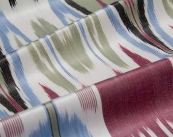 May include: Close-up of a folded fabric with a white background and a pattern of brushstrokes in black, blue, green, and burgundy. The fabric has a silky sheen and a flowing drape, suggesting it is a decorative textile.