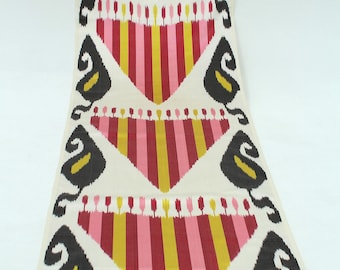Könnte beinhalten: Weißer Stoff mit einem sich wiederholenden Muster aus schwarzen, rosa und goldenen Streifen und Blattformen. Der Stoff hat ein traditionelles Ikat-Design.