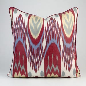 May include: Red, blue and cream patterned throw pillow with a geometric design. The pillow is made of a soft, woven fabric.