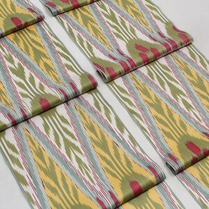 May include: Close-up of folded fabric with a green, yellow, white, and red ikat pattern. The fabric is folded in a way that shows the pattern repeating.