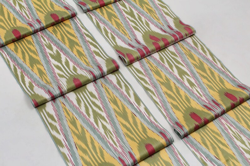 May include: Close-up of folded fabric with a green, yellow, white, and red ikat pattern. The fabric is folded in a way that shows the pattern repeating.