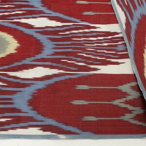 Pu&ograve; includere: Primo piano di un tessuto con motivo rosso, bianco e blu con un design ikat ripetuto. Il tessuto ha una consistenza morbida e testurizzata.