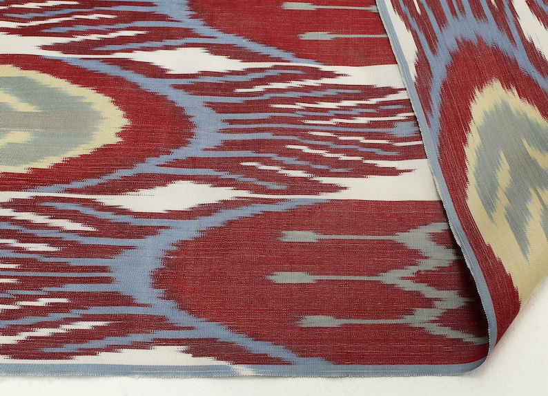 Pu&ograve; includere: Primo piano di un tessuto con motivo rosso, bianco e blu con un design ikat ripetuto. Il tessuto ha una consistenza morbida e testurizzata.