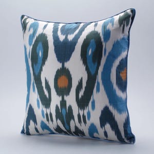 Könnte beinhalten: Ein weißes Kissen mit einem blauen und grünen Ikat-Muster. Das Kissen hat einen dezenten orangen Akzent in der Mitte.