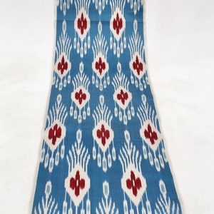 Può includere: Un tessuto blu con un motivo ikat bianco e rosso. Il motivo presenta un disegno ripetitivo di fiori e foglie stilizzati.