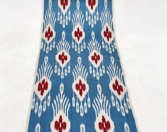 May include: A blue fabric with a white and red ikat pattern. The pattern features a repeating design of stylized flowers and leaves.