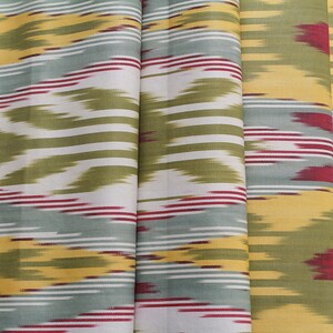 May include: A fabric with a repeating pattern of yellow, green, white, and red stripes. The fabric has a subtle ikat design.