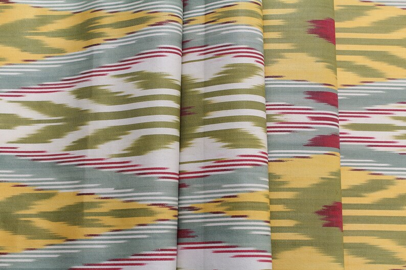 May include: A fabric with a repeating pattern of yellow, green, white, and red stripes. The fabric has a subtle ikat design.