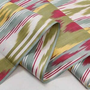 May include: A close-up of a fabric with a striped pattern in shades of green, blue, yellow, and red. The fabric is folded and has a soft, textured feel.