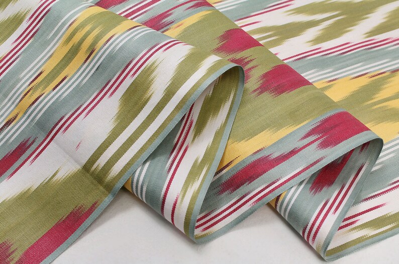 May include: A close-up of a fabric with a striped pattern in shades of green, blue, yellow, and red. The fabric is folded and has a soft, textured feel.