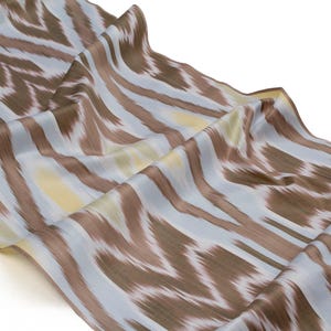 May include: A flowing fabric with a repeating pattern of brown and white brushstrokes over a light blue background. The fabric is draped, showing the texture and sheen of the material. The overall effect is a soft, abstract design.