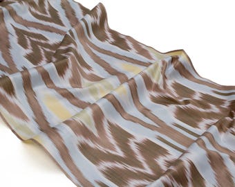 May include: A flowing fabric with a repeating pattern of brown and white brushstrokes over a light blue background. The fabric is draped, showing the texture and sheen of the material. The overall effect is a soft, abstract design.