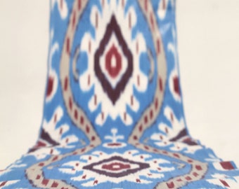 May include: A blue and white patterned textile with a repeating design in shades of blue, white, gray, and burgundy. The fabric is draped, showcasing the intricate pattern and color variations. The textile appears to be lightweight.