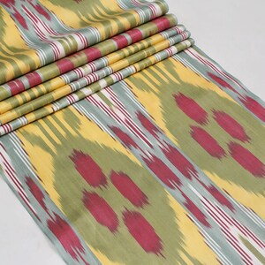 May include: A close-up of a fabric with a yellow, green, and red ikat pattern. The fabric is folded in several layers, showing the pattern repeating.