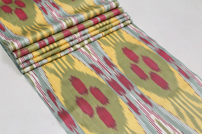 May include: A close-up of a fabric with a yellow, green, and red ikat pattern. The fabric is folded in several layers, showing the pattern repeating.