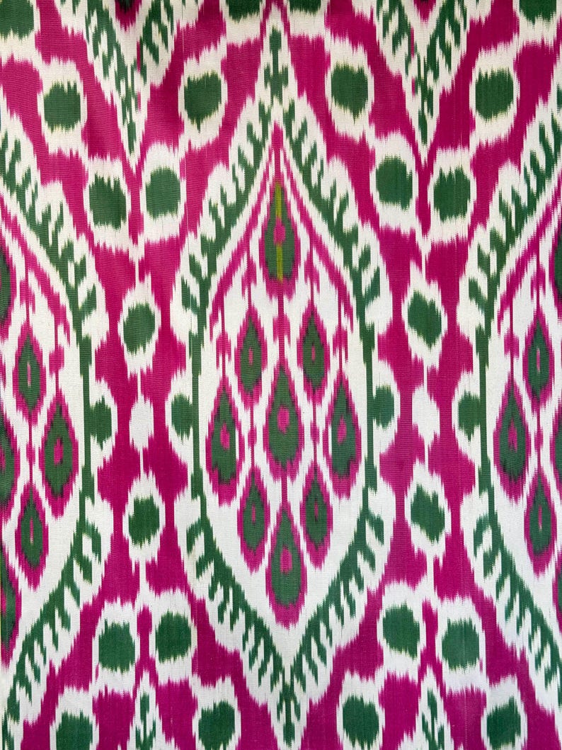 May include: A vibrant textile featuring a repeating pattern of stylized teardrop and oval shapes. The design incorporates shades of fuchsia, green, and white, creating a bold and eye-catching visual effect. The fabric's intricate pattern suggests it could be used for upholstery or apparel.
