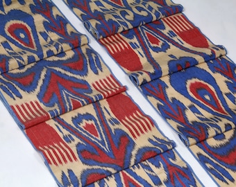 May include: Two pieces of fabric with a traditional ikat pattern in shades of blue, red, and beige. The fabric is folded and has a woven texture.