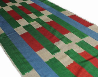 May include: A woven fabric with a striped pattern in shades of green, red, blue, and beige. The fabric has a subtle ikat design.