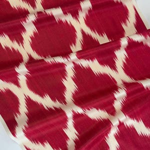 Può includere: Primo piano di un tessuto rosso con un motivo astratto color crema. Il tessuto è piegato, mostrando la trama e il design. Il motivo è composto da forme e linee irregolari, creando un tessuto visivamente interessante.